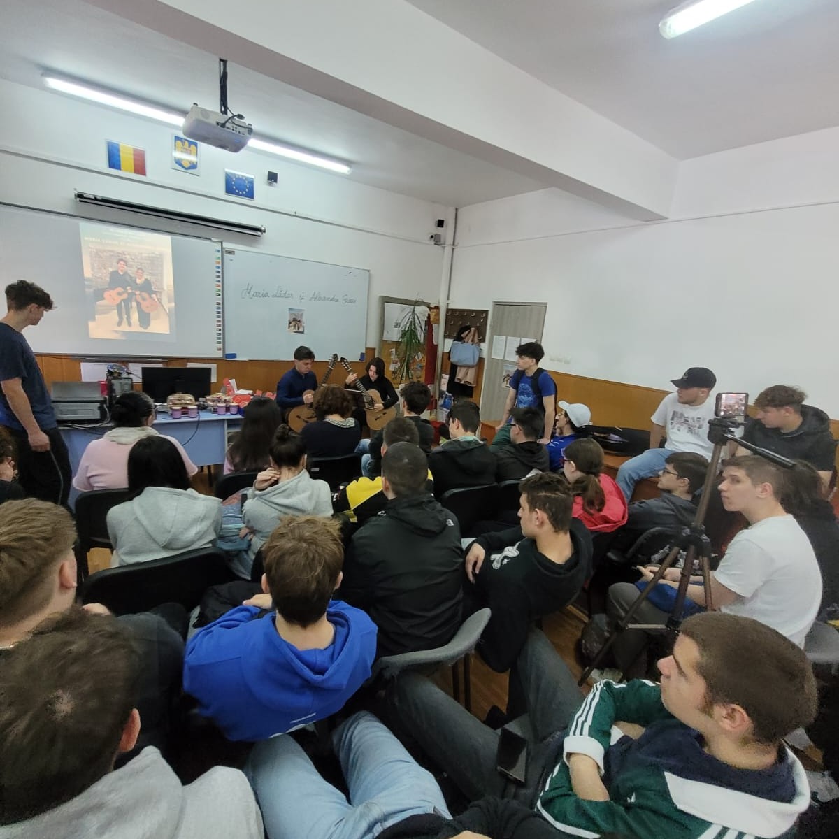 Cei doi chitariști interpretează în fața unei săli pline